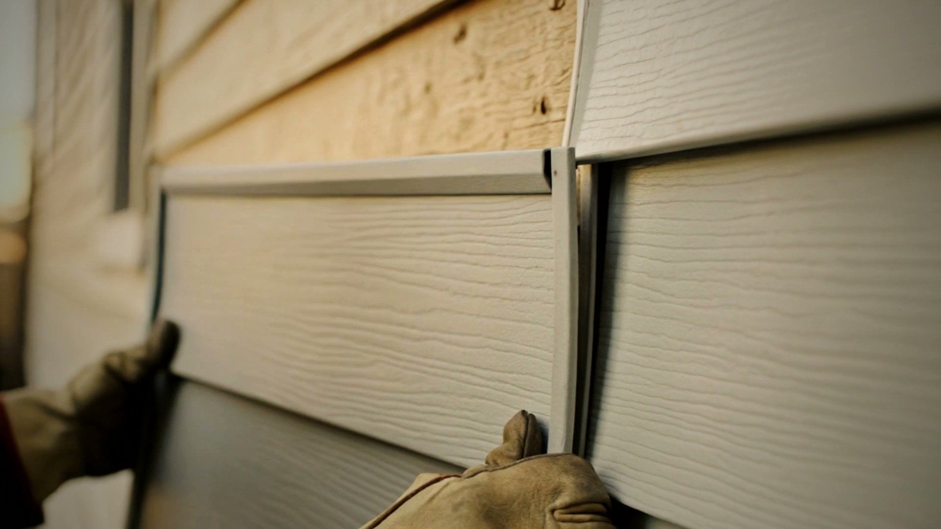 A gloved hand fitting a course of new lap siding